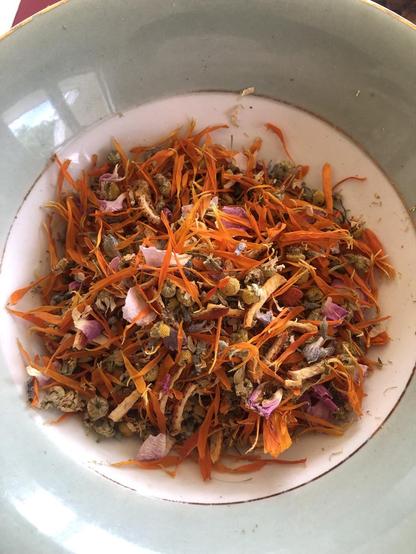 All dried ingredients in a bowl to mix. A vintage breakfast bowl with a gold rim with dried herbs. They are a mixture of orange, yellow, pink and white.