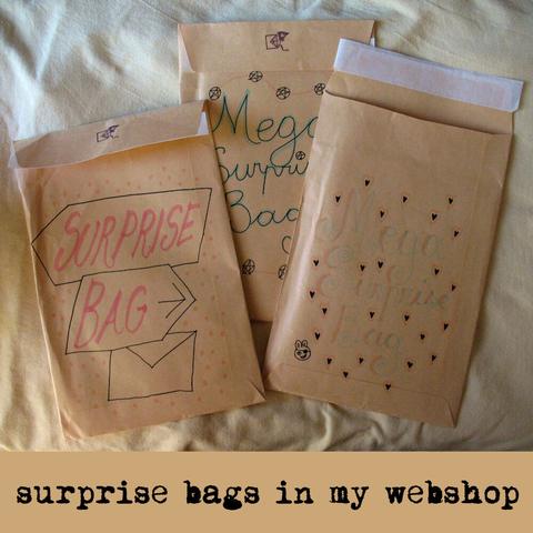 Photo of 3 beige envelopes with "surprise bag" and "mega surprise bag" handwritten on them in different font styles, decorates with arrows, pentagrams, and hearts. Text: surprise bags in my webshop.