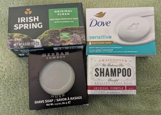 four bars of soap products, Bath soap (Irish Spring), Face Soap ( Dove), Shaving Soap (Herban), Shampoo (J.R.Liggett's) Shown to illustrate the elimination of plastic containers.