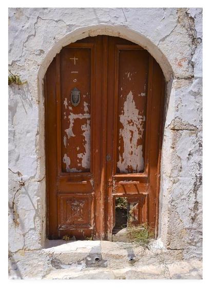 Portrait colour photograph of a battered old brown wooden door within a white plastered archway.