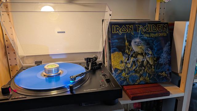 Eine blaue Schallplatte liegt auf einem Plattenteller. Daneben steht das Cover mit dem Schriftzug Iron Maiden. Ebenso sieht man das Maskottchen Eddie darauf abgebildet