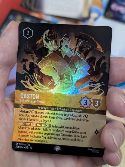 Close-up of a shiny epic Lorcana card of the character Gaston. It has a rainbow foil effect and is a yellow card.
