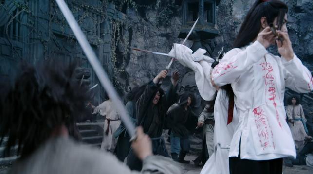 Wei Wuxian (actor Xiao Zhan) (in white shirt (with red writing) playing a dizi while Lan Wangji (actor Wang Yibo) (in white robes) is fighting around him with a sword to keep the puppets away.