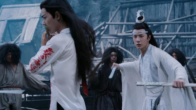 Wei Wuxian (actor Xiao Zhan) (in white shirt (with red writing) playing a dizi while Lan Wangji (actor Wang Yibo) (in white robes) is fighting around him with a sword to keep the puppets away.