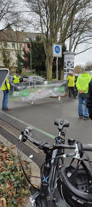 Menschen halten ein Transpi quer über den RS1 auf dem steht macht diesen Radweg endlich schnell.
Der Hintergrund ist ein Radweg, über den eine überdimensionale Schnecke kriecht