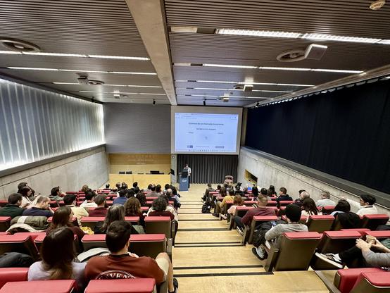 Georgiana Frincu en el escenario del auditorio de la a11yConf 2025 en Gerona hablando de marcaje para accesobilidad delante de la audiencia, en un plan más amplio con la sala llena de asistentes
