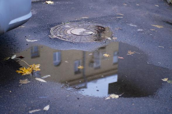 Reflection of the top of a yellow Stalin-era building in a puddle with yellow maple leaves on it, focused on the leaves and the puddle, in a courtyard on vulica Kirava in Minsk, Belarus on an October day in 2025