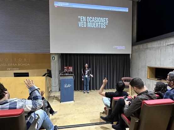 Mia Salazar en el escenario del auditorio de la a11yConf 2025 en Gerona hablando de atributos ARIA delante de la audiencia, en un plan más amplio con la sala llena de asistentes