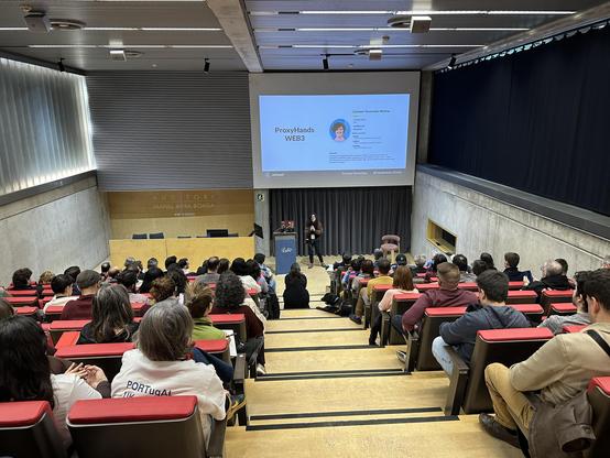 Carmen Torrecillas en l'escenari de l'auditori de l'a11yConf 2025 a Girona parlant de visualitzacio de dades accessible davant de la audiència, amb un pla més ampli amb la sala plena d'assistents
