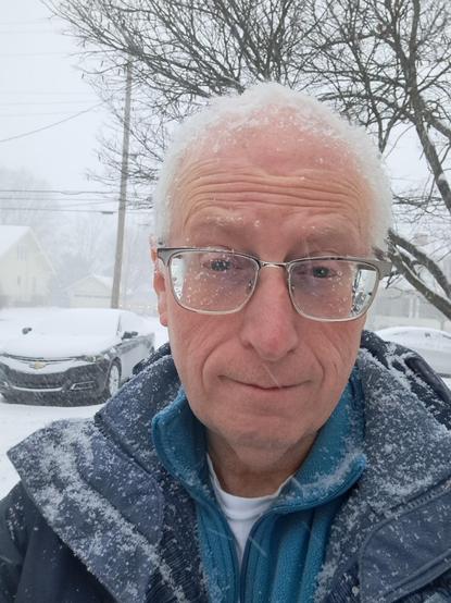 selfie of me, a little scowly, covered in snow, with a winter wonderland behind me