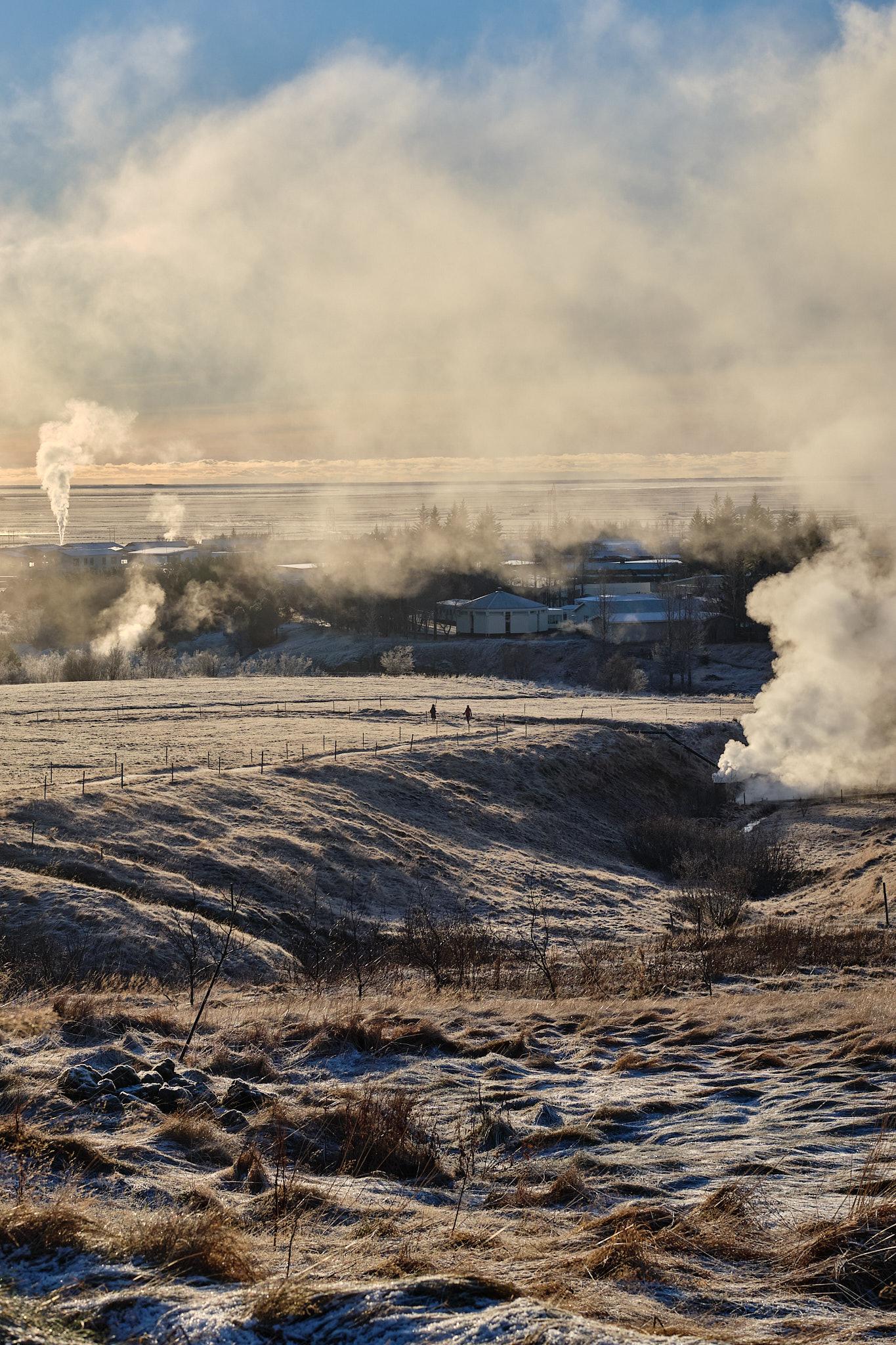 Two people meet while out on a walk through a field with steam plumes on either side.