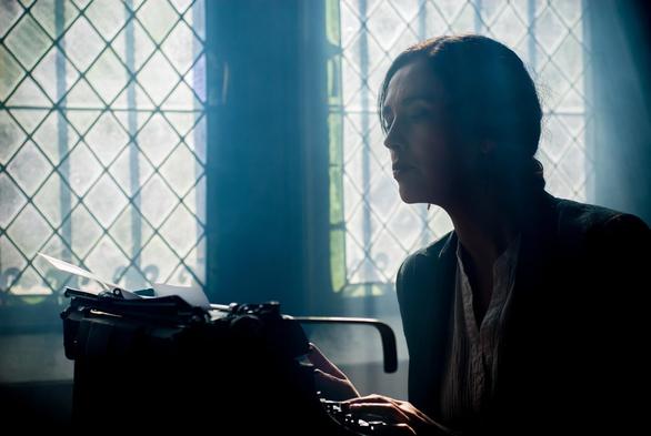 Writer using a vintage typewriter by a window with stained glass, bathed in dramatic sunlight.