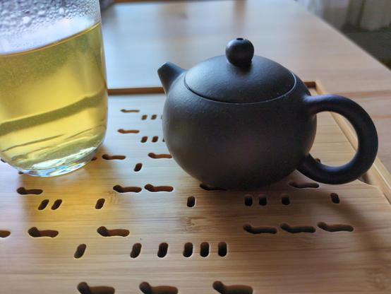 A Yixing Zini Black Gold teapot in the Xishi style. It is tiny, about the size of the palm of my hand!

It's almost spherical, made of an unglazed dark brown clay, with a tiny little spout.

It sits on a bamboo tea tray, next to a glass fairness jug with some amber sheng puerh tea in it.