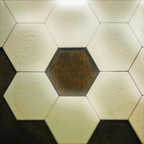 White hexagon tiles loosely form around an empty hexagonal space, revealing dark brown wood backing underneath.