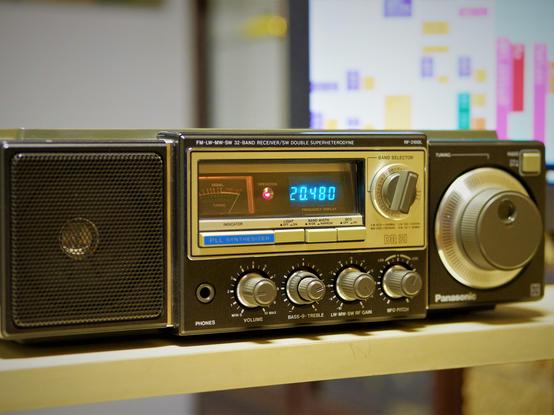 Photo of my shortwave radio receiver. A Panasonic beast from 1986 with numerous rotary controls, an illuminated signal level meter and a flourescent digital display.