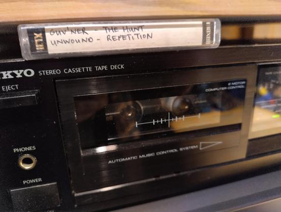 Photo of a cassette on top of a cassette player. The cassette says "Guv'ner - The Hunt" and "Unwound - Repetition" on the side.