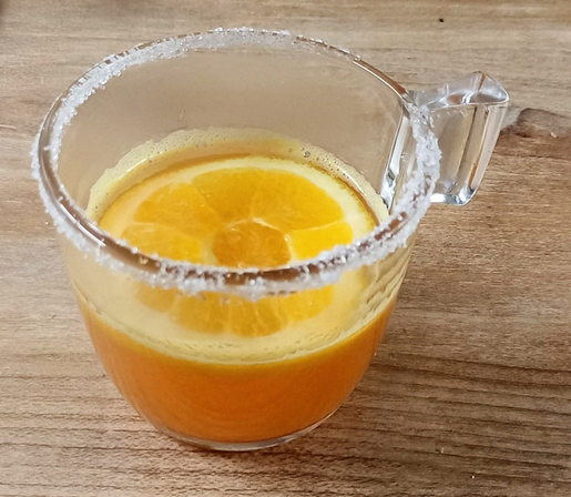 in einer Glastasse mit Zuckerrand eine orangene Flüssigkeit, darin schwimmt eine Orangenscheibe.