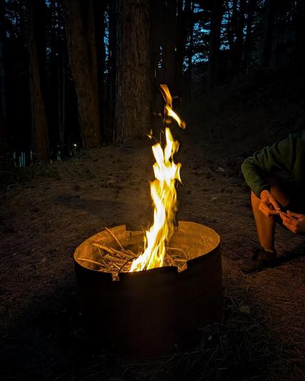 A person sits by a fire brazier in the woods