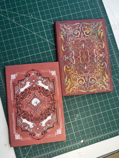 Two notebooks, handbound, with fantasy-themed ornamental designs.