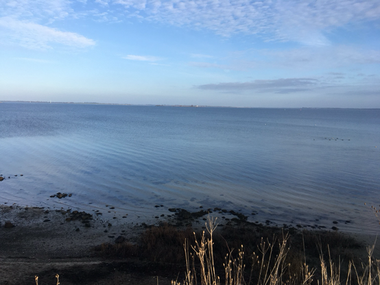 Blick vom Steilufer über die ruhig daliegende Ostsee auf die Insel Poel . Blauer Himmel mit einigen, wenigen Wolken.