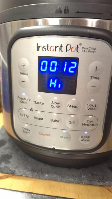 Detailaufnahme des Bedienfeldes mit einem Display, das die Zahl 12 Minuten und die Buchstaben "Hi" anzeigt sowie diversen Knöpfen. Die Knöpfe "Pressure Cook", "Start" und "Keep Warm" leuchten.