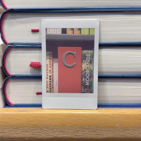 Instant photo of a big c letter next to books in front of a pile of books.