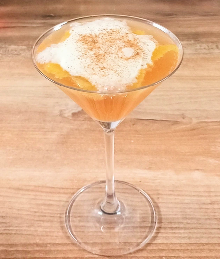 ein Martiniglas mit einer Orange-gelben Flüssigkeit, bedeckt mit einer Sahneschicht und mit Zimt gepudert.
