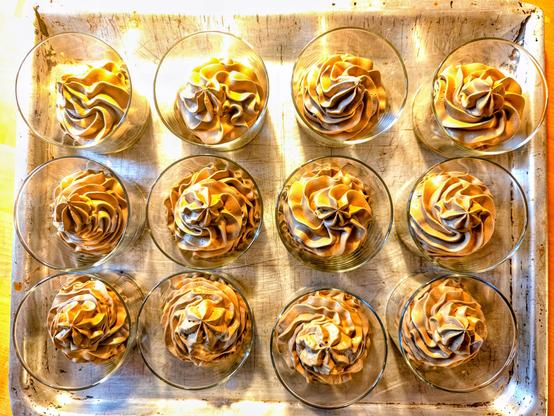 Auf einen Backblech stehen drei mal vier Wassergläser. Sie sind von oben fotografiert. Sie enthalten mit einer Sterntülle eingespritzte Mousse au Chocolat.