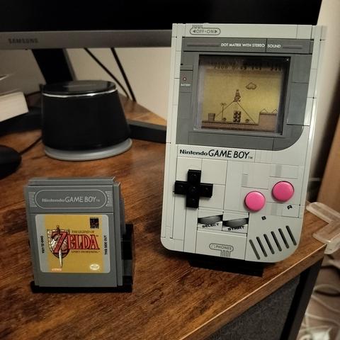 A LEGO Gameboy and a LEGO Legend of Zelda cartridge next to it. The LEGO Super Mario Cartridge is inserted and the screen display shows a gameplay snippet of the Super Mario game.
