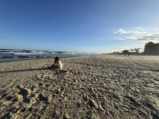 foto: beira mar em praia do rio grande do sul, em uma imensa faixa de areia há apenas uma menina brincando, ao entardecer, a menina está de costas, e em sua frente o mar