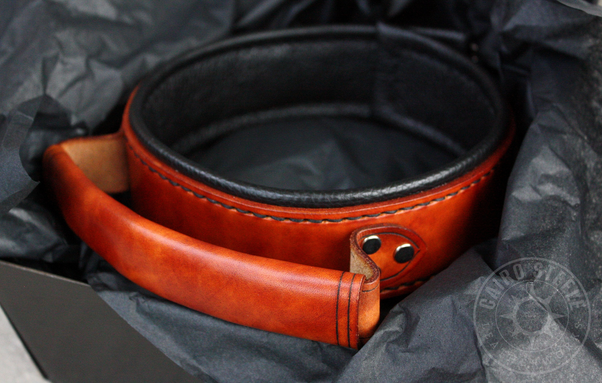 A brown leather collar with a black liner and a handle riveted to the front
