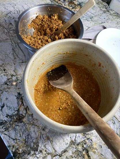 We see a luxurious orange paste in a brown crock. The wooden label handle is pointing to fiveoclock.