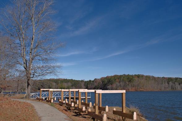 A lakeview with blue sky and streaks of clouds. A barren tree on the left, and an empty kayak rack at the bottom.