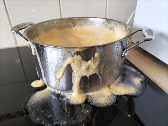 Stainless steel cooking pot with overflowing yellowy apricot jam on a black induction cooktop