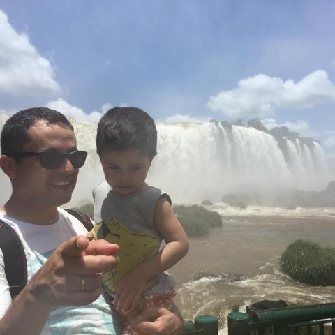 homem com criança pequena no colo, ao fundo as cataratas do iguaçu