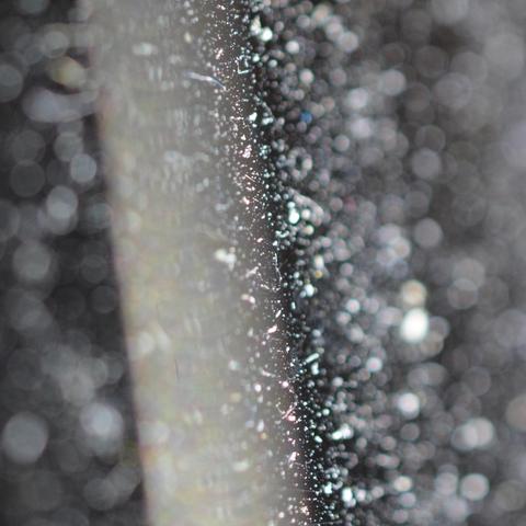 Very abstract-looking close-up of an electric guitar string with lots of circles of confusion from dust on the dusty guitar. Nothing in focus. The string runs from top to bottom just to the left of center.
