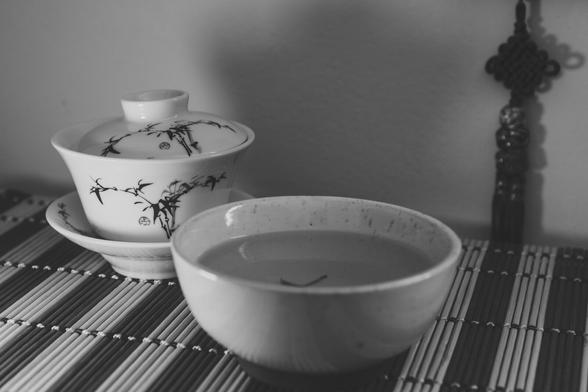 a chinese gaiwan (cup with a lid) and a bowl of tea on a striped tea mat