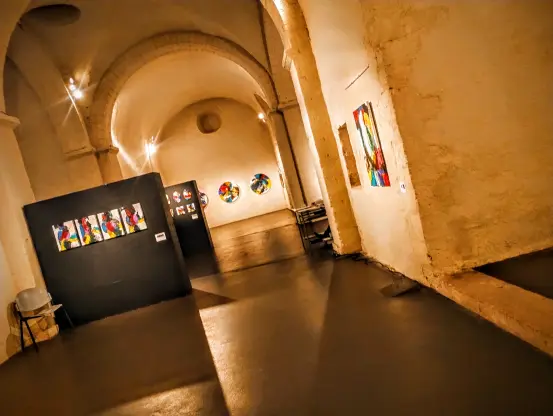 Ancienne chapelle aux éclairages tamisés accueillant une exposition de toiles abstraites.