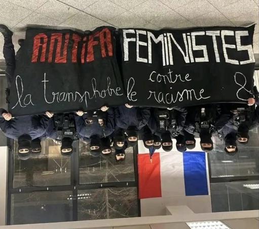 Image à l’envers d’un groupe de policiers cagoulés avec un drapeau français derrière eux. Ils posent derrière une bannière de manifestation retournée sur laquelle on peut lire « antifa féministes contre la transphobie et le racisme ».