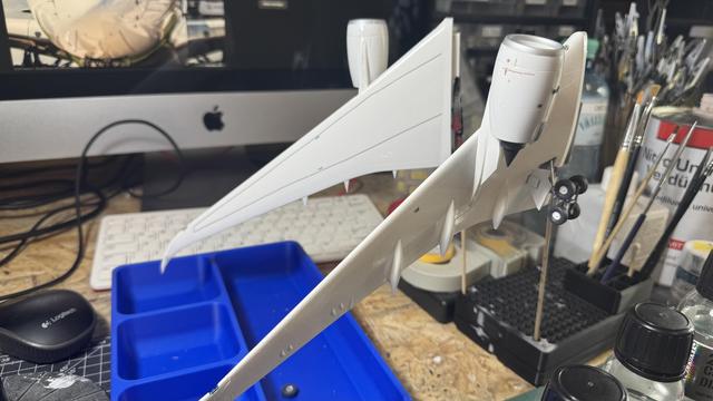 Side view of a white model airplane wing with landing gear extended, set against a background of a computer keyboard and painting tools.