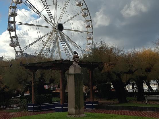 Se ve una paloma encima de una estatua. Se ve al fondo una noria