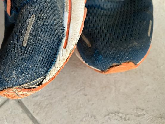 Blauer Sportschuh mir orangener Sohle. Das Gewebe ist auf 5 cm von der Sohle abgerissen.