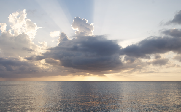 a sunset includes pastel yellows, blues, greys and whites. crepuscular, God rays appear from the clouds, which extend over a flat, calm, reflective sea