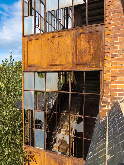 A rusted industrial structure with broken windows revealing a staircase inside.