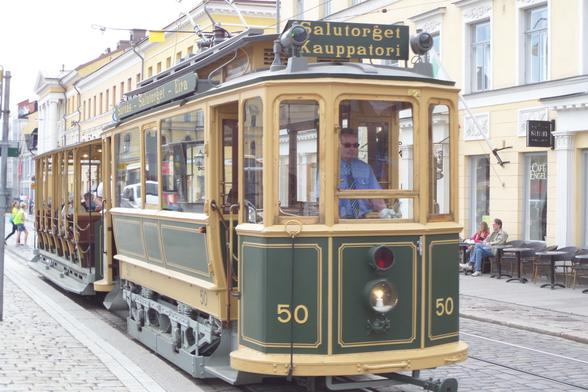 A green and cream-coloured trolley car/tram driving along a European street. The tram's sign says "Salutorget Kauppatori"