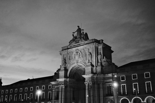 BW picture of the Rua August Arch at Dawn. The surrounding historical building windows are lit up with Christmas lights.