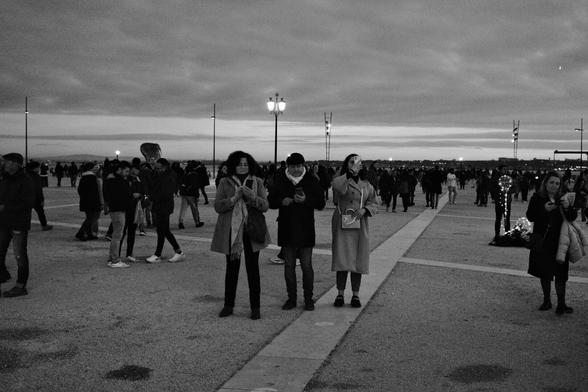 BW picture of the crowded square, on an overcast afternoon. In the center of the picture three people taking pictures and looking at their phones.