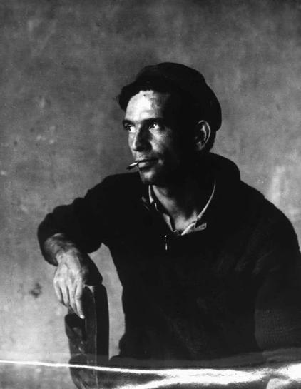 A black and white photograph depicts a person with an intense gaze. They are wearing what appears to be a dark sweater or jacket, possibly with some texture that suggests it might have been used clothing, indicative of hard work or labor-intensive occupation given the visible wear on their sleeve.

The individual is holding onto something in their left hand which seems like part of machinery; perhaps they're operating an industrial machine. This contributes significantly to conveying a sense of physical strength and resilience. They are also seen with what looks like smoking, possibly reflecting on life's hard moments or taking breaks during strenuous tasks.

There’s evident contrast between light and shadow in the image accentuating textures and creating depth which can be indicative of the artist wanting to capture not just an individual but their inner world as well. The background is nondescript, a plain surface that does nothing to distract from the subject's story. 

This photograph comes with historical context tied to the Italian migration during mid-20th-century post-war Europe - particularly around 1963 when this was published by Loener N.V., an Amsterdam-based publishing company known for its focus on documenting immigrant life in Italy and related communities.

The title "Immigrato" suggests a narrative of displacement, integration struggles or perhaps the struggle to find one's place within new circumstances [...]