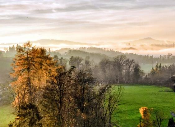Aerial from a plain with autumn colored trees and the mist rolling in between distant hills