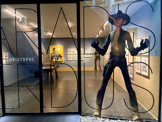 Glasfront mit comichaften Cowboy. Dahinter Blick in die Ausstellung